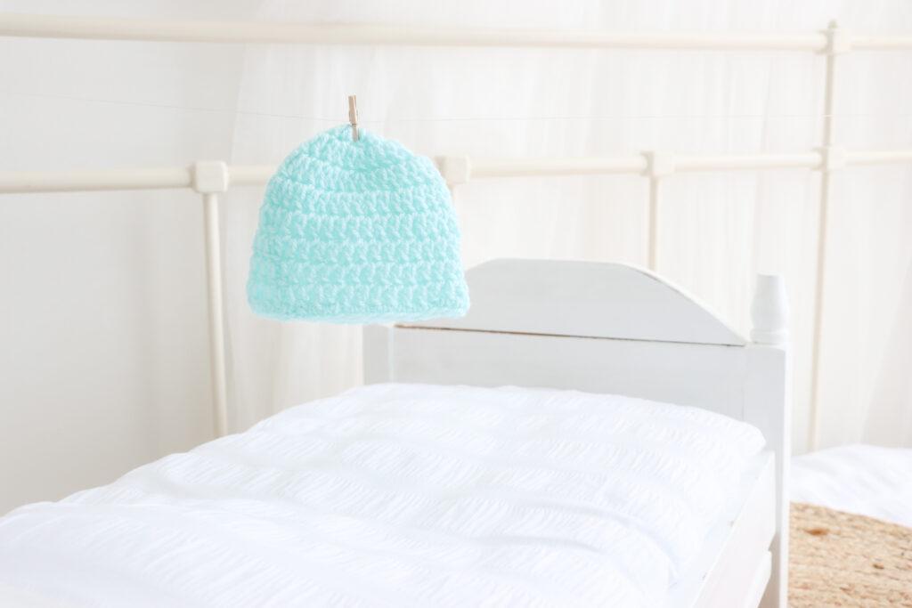 a turquoise baby beanie pegged up on fishing line in a white bedroom setting