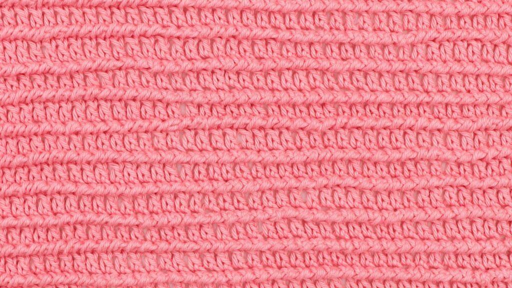 Close-up of a crocheted swatch using the corded ridge stitch in bright pink yarn, showing horizontal textured ridges and evenly spaced rows.