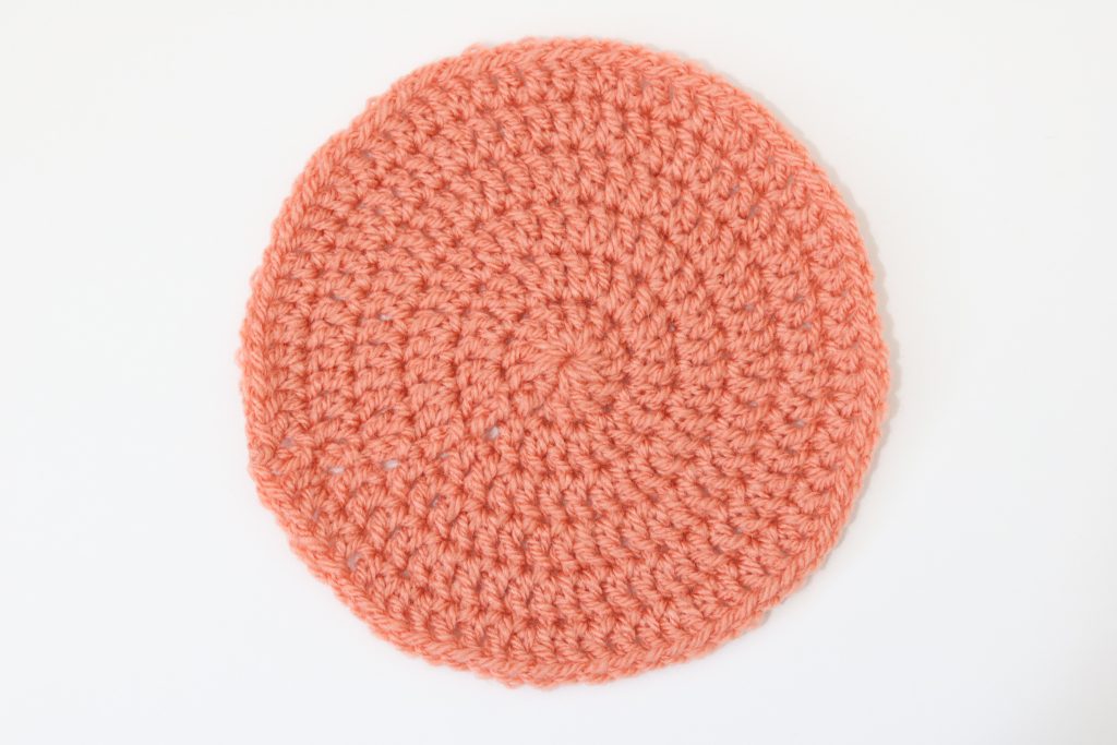 a flat lay image of a crochet flat circle made in orange yarn on a white background