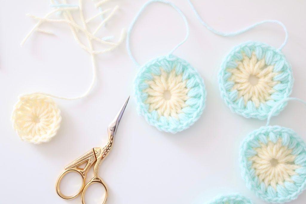 The beginnings of four sunburst granny squares sit on a white background alongside some gold scissors.
