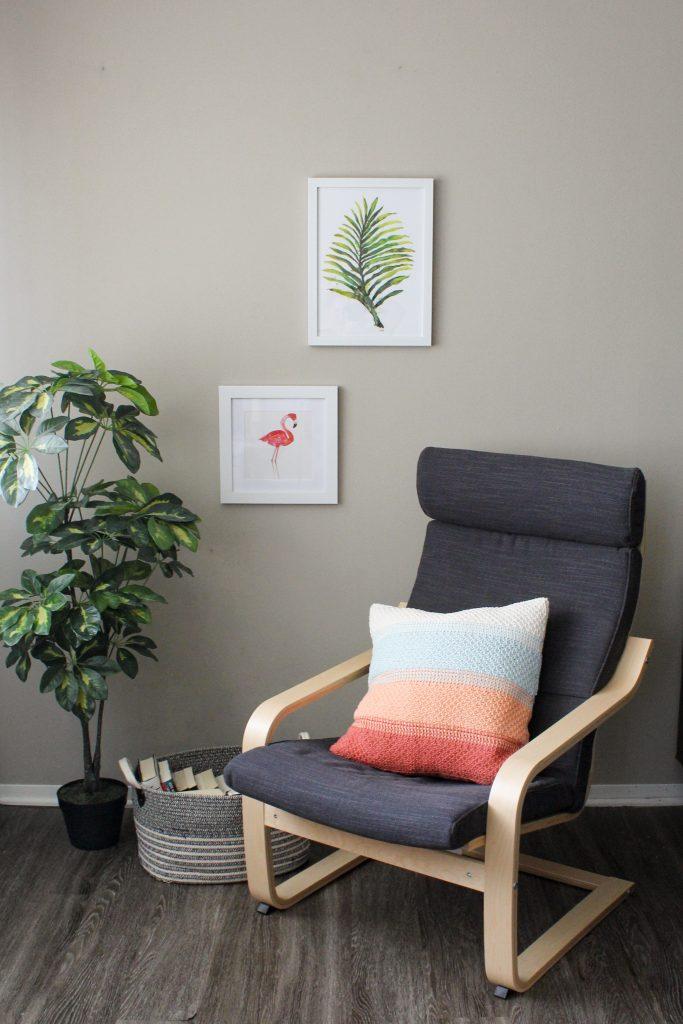 A Tunisian crochet pillow sits on a grey chair beside a green plant
