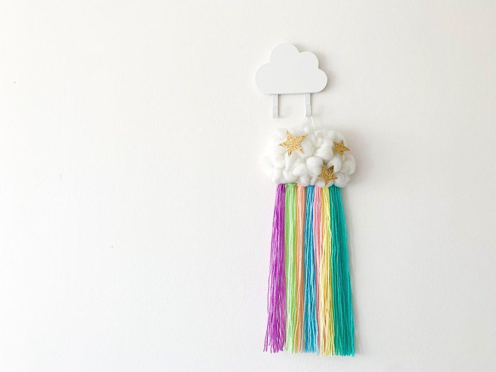 Rainbow wall hanging with a cloud and tassels hung on a white wall.