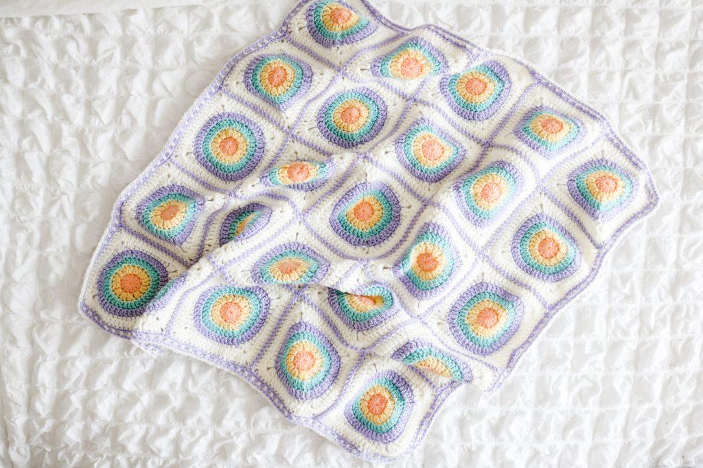 Cream blanket with pastel rainbow circles on a white bed.