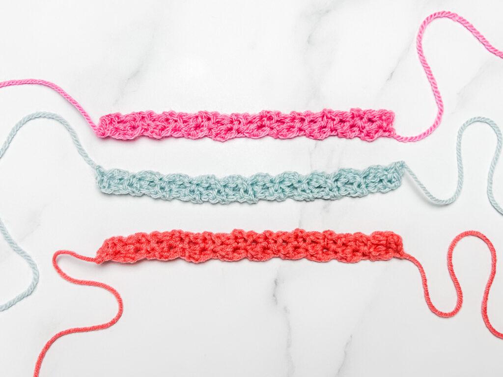 flay lay image of three crochet friendship bracelets in three colours, pink, pale blue and orange lay on a white marble backdrop.