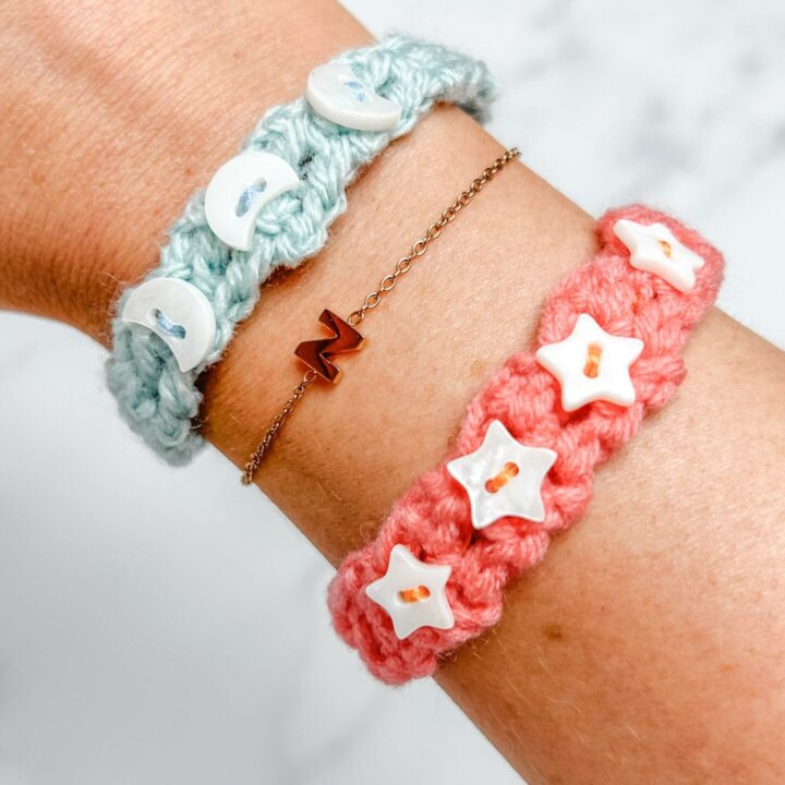 females wrist wearing two crochet friendship bracelets one orange and one pale blue embellished with white moon and star beads.