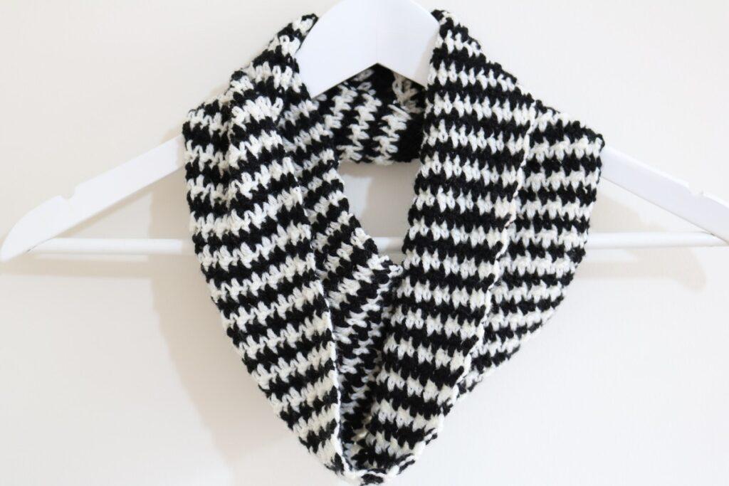 A black and white cowl in the houndstooth check pattern is wrapped around a hanger