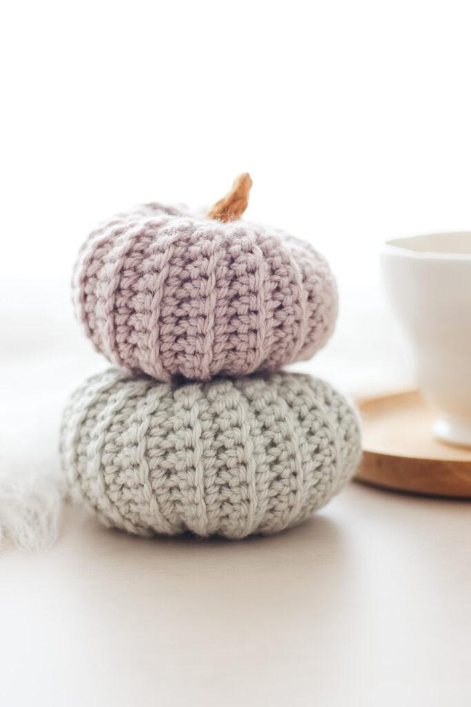 two crochet pumpkins stacked. The top pumpkin is made in a mushroom yarn and the bottom pumpkin is made using a light grey yarn.