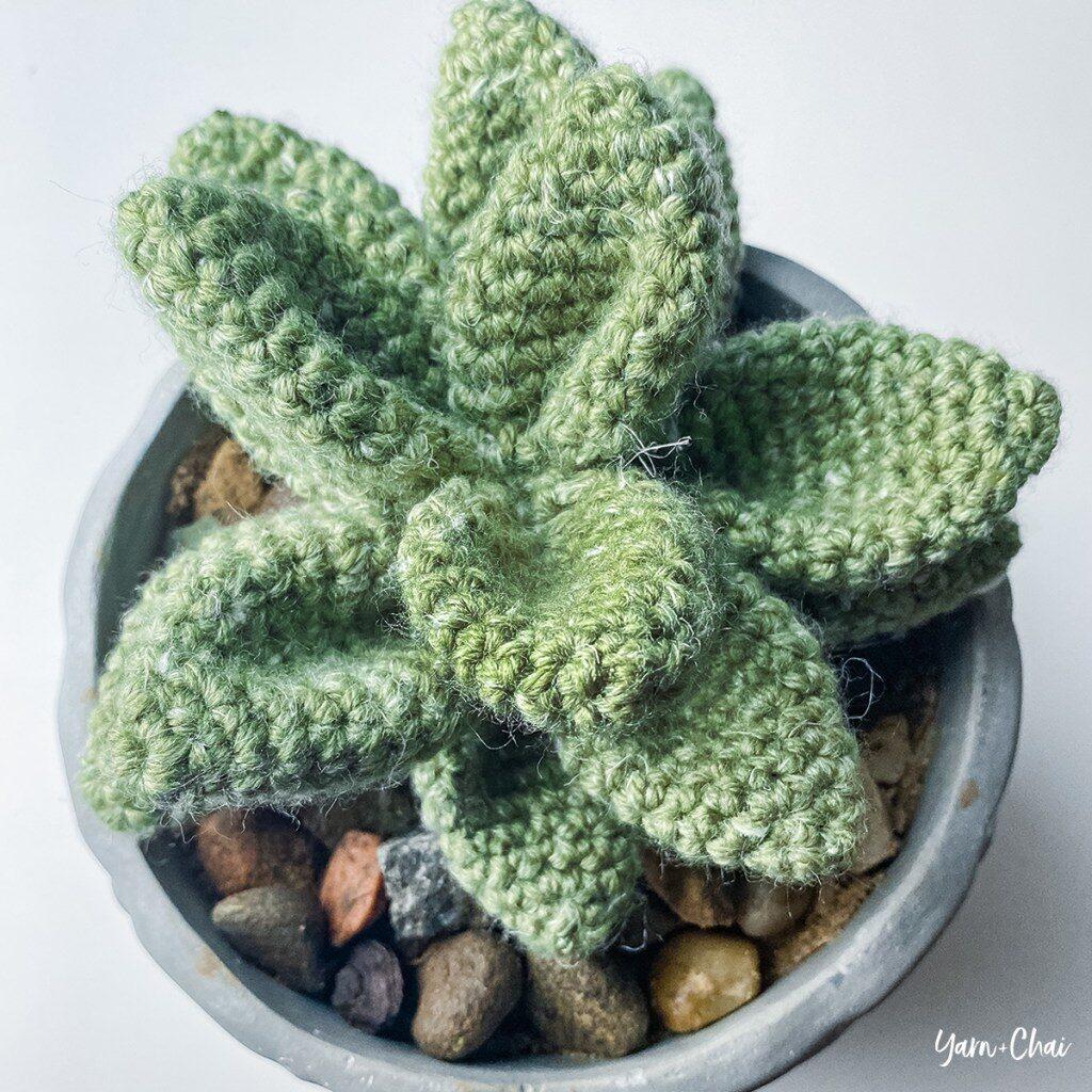 A green succulent made of yarn sits in a grey plant pot.