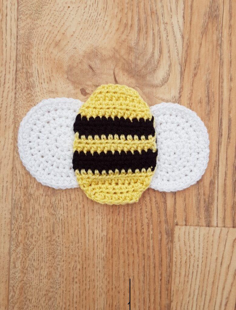 A crochet bee made from black, yellow and white yarn sits on a wooden background.