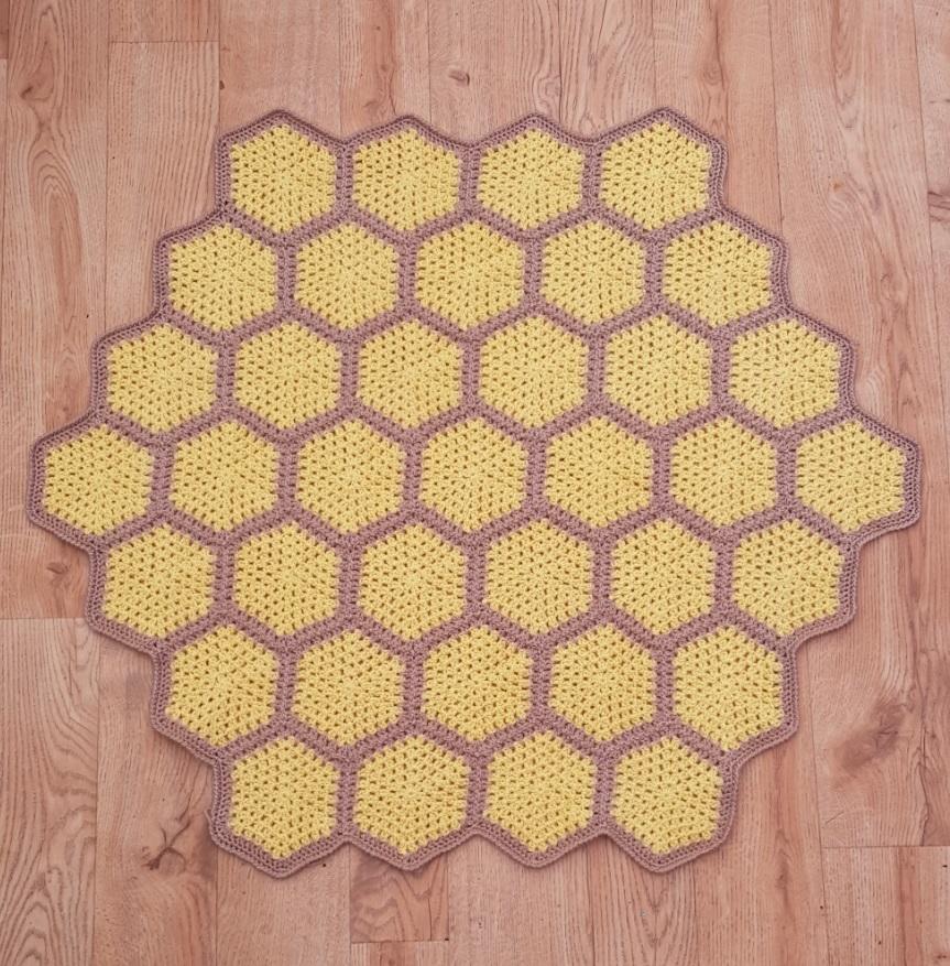 A bee crochet blanket in shades of yellow and brown sits on a wooden floor. There are yellow hexagons, but the bees are still to be added.