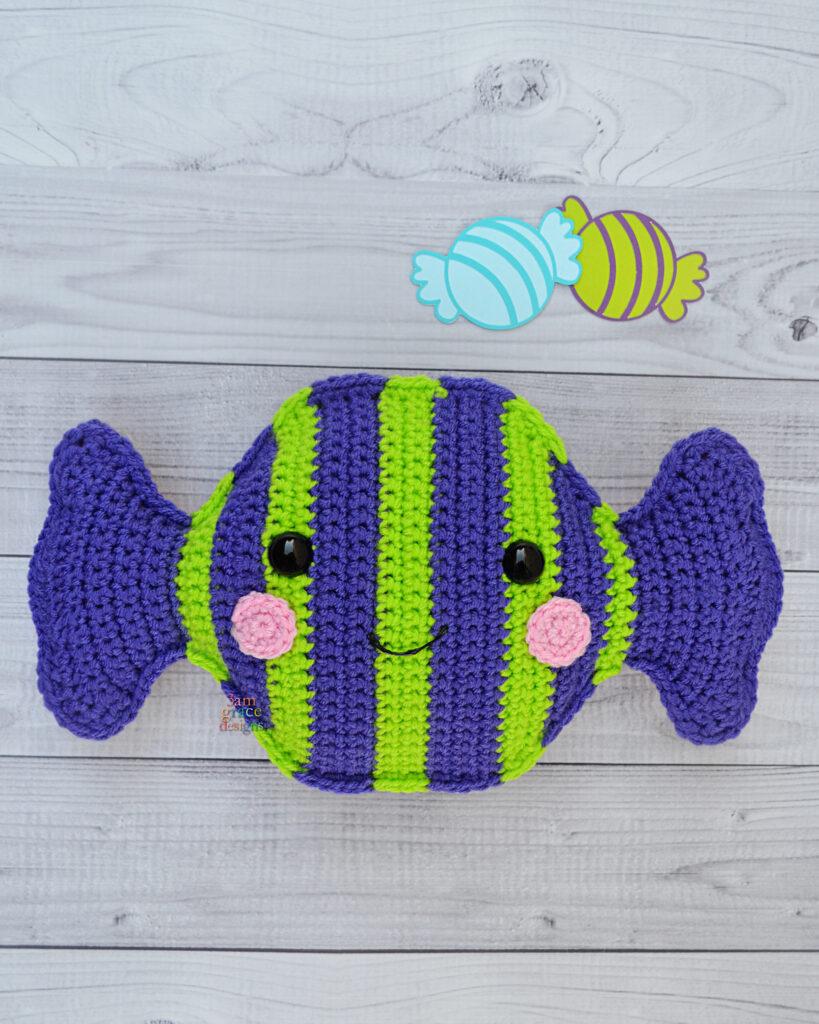 A crocheted candy in vibrant shades of purple and lime stripes sits on a wooden floor.