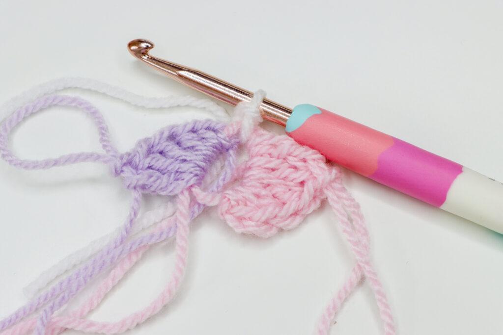 A spiral granny square in pastel pink, purple, grey and white is in progress.