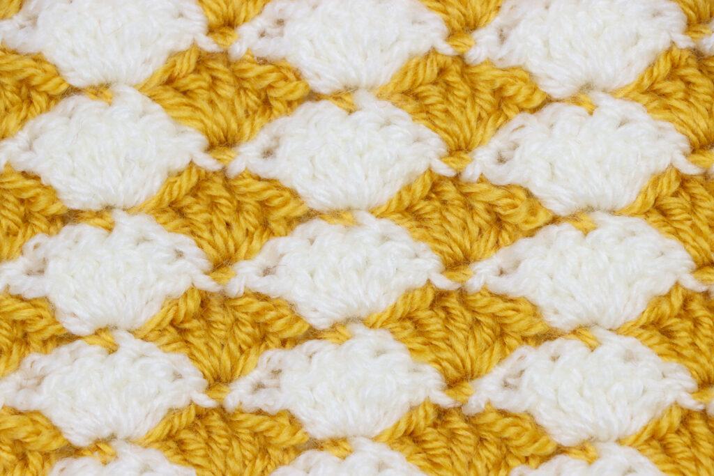 A swatch of crochet shell stitch in mustard and white yarn.