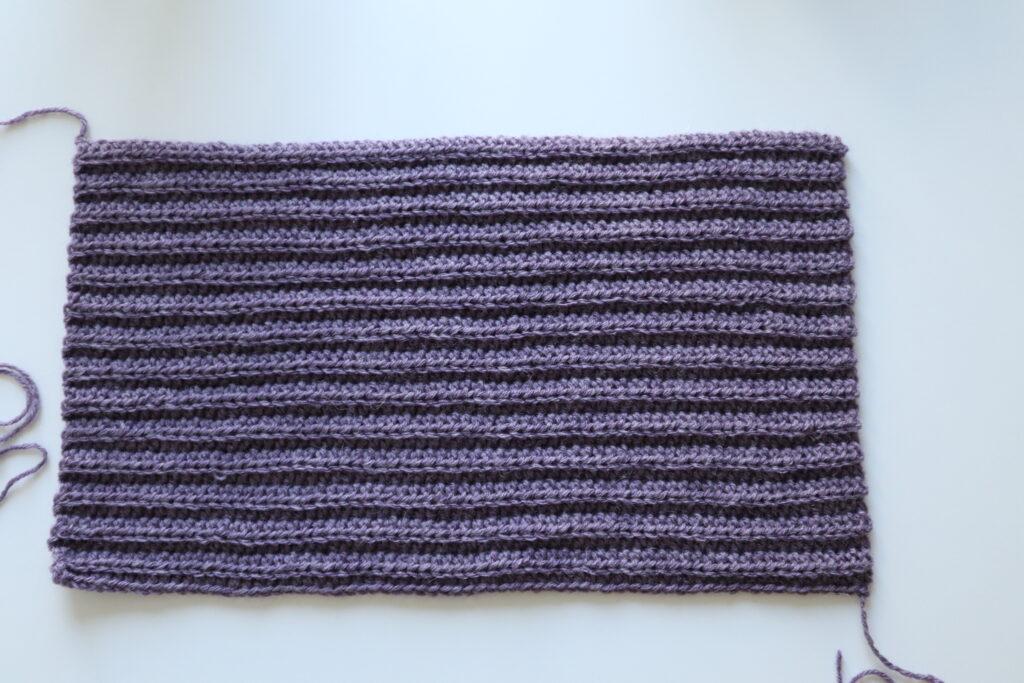 A swatch in purple yarn showing the construction of the crochet cardigan