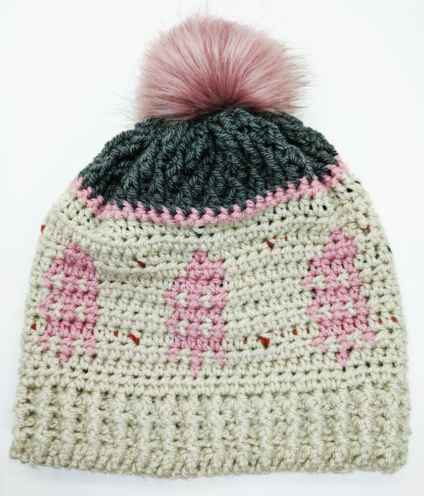An alpine themed crochet hat in shades of cream, pink and grey is topped by a pink pompom.