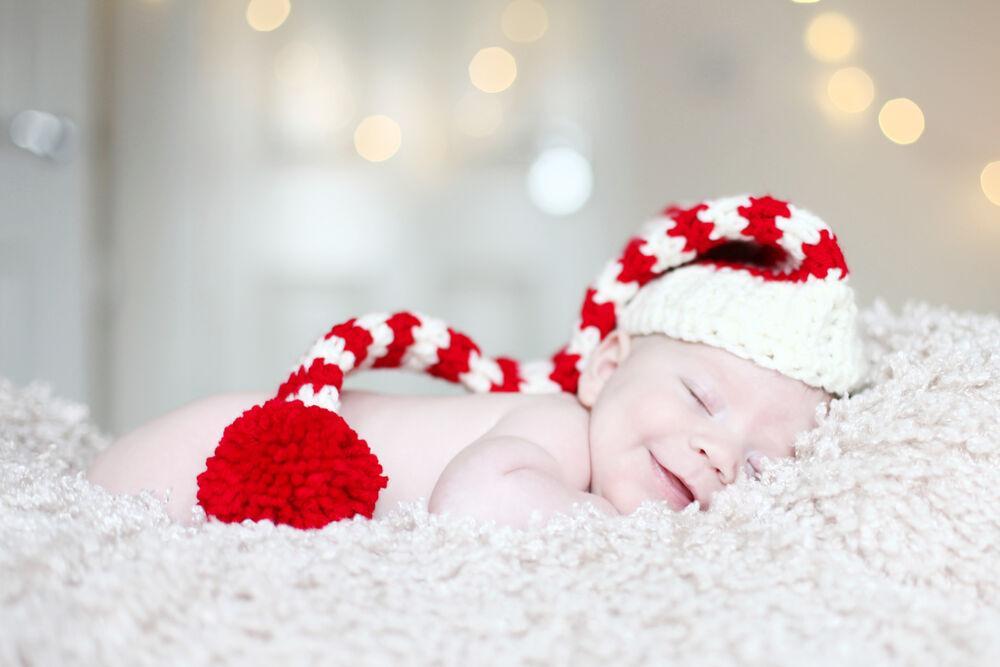 young baby lay on a fluffy blanket wearing a red and white striped crochet elf hat