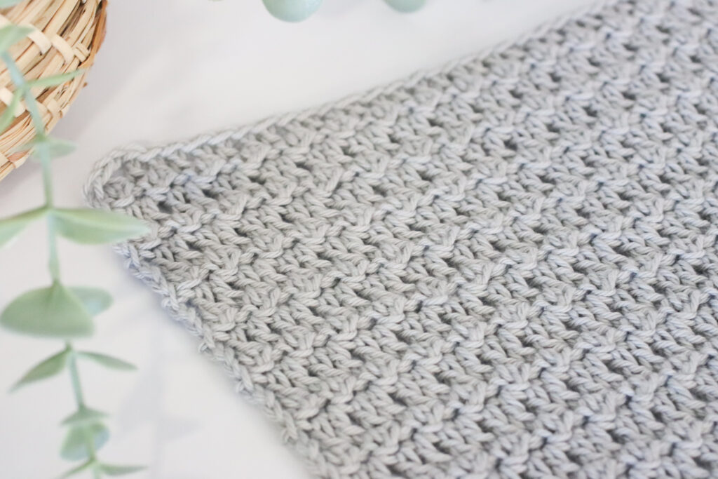 a grey crochet swatch of the floret stitch on a marbled backdrop and foliage to the left of the image.