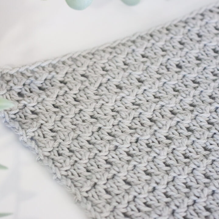 Floret stitch in grey yarn on a white background next to a plant.