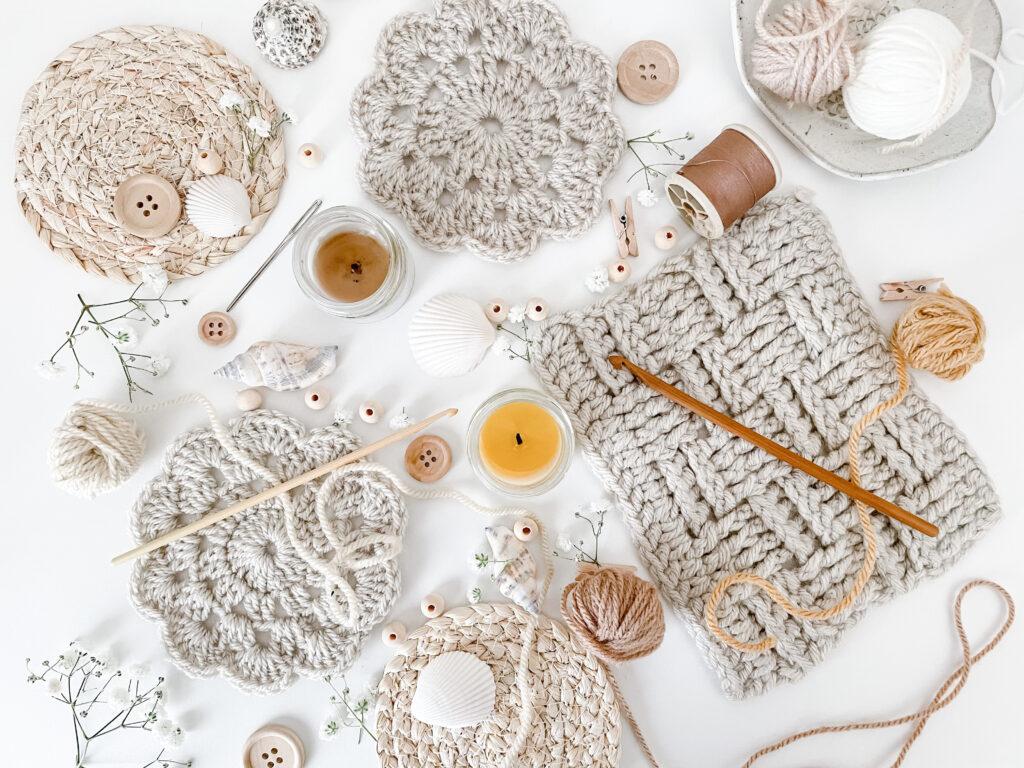 a flat lay image of neural, beige and cream objects including a coaster, swatch of the basket weave stitch, shells, wooden buttons, beads and wooden crochet hooks.