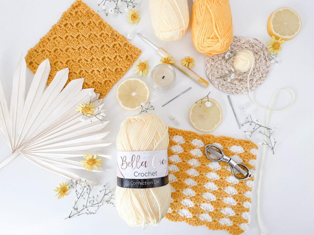 a flay lay image of yellow objects including two crochet swatched, yarn, slices of lemon and yellow flowers.