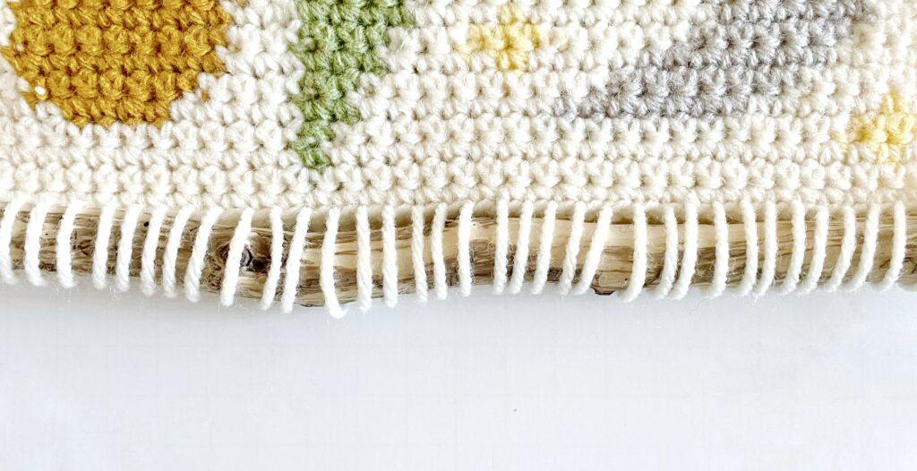 A tutorial graphic showing the wall hanging attached to the wooden hanger.