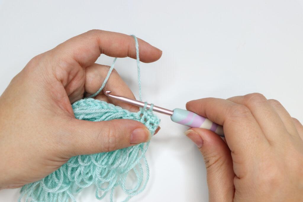 An in progress swatch of crocheted loop stitch in aqua yarn.