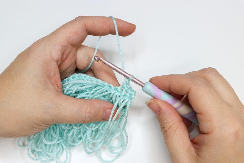 An in progress swatch of loop crochet stitch in aqua yarn.