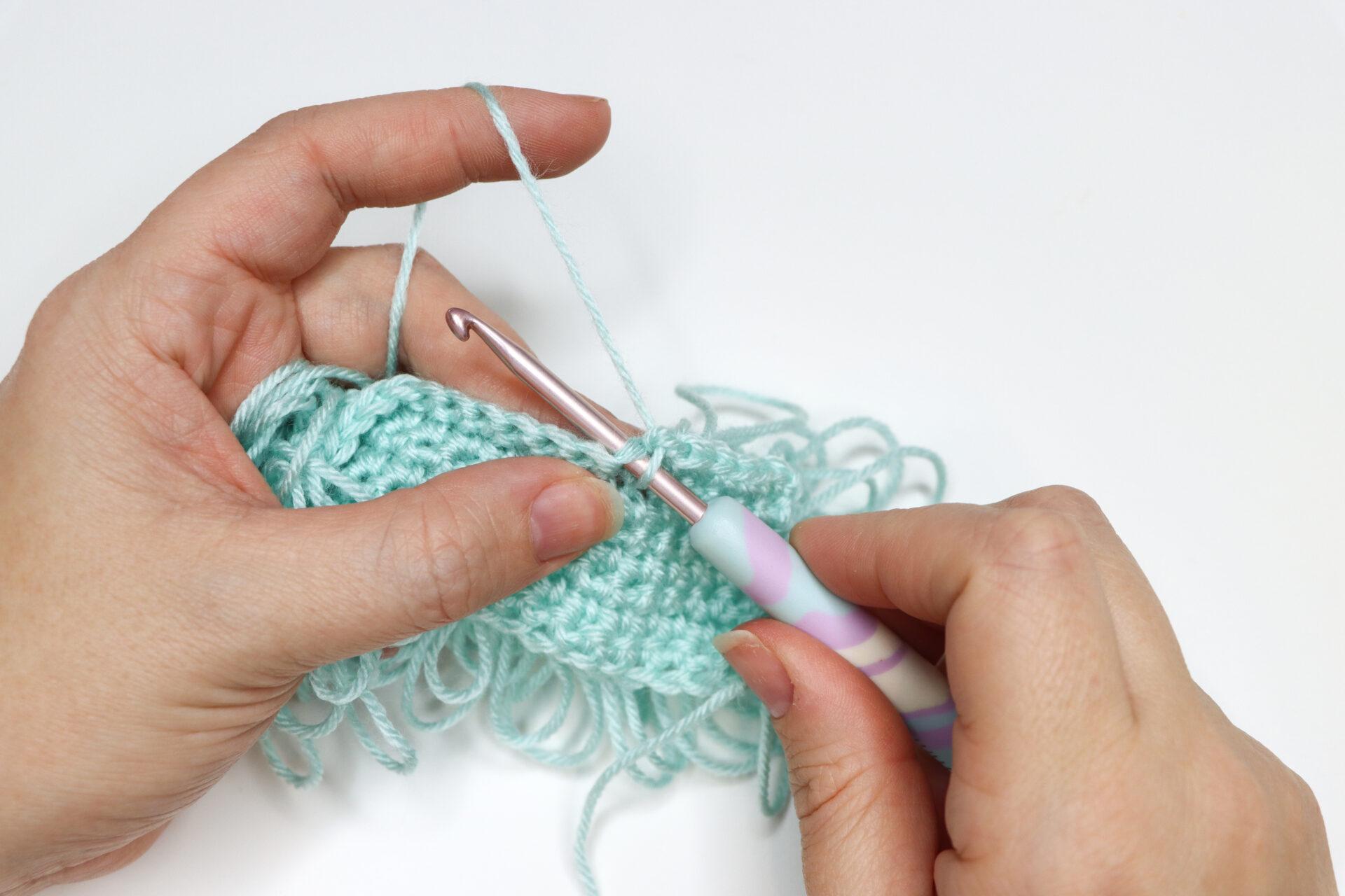 An in progress swatch of loop crochet stitch in aqua yarn.