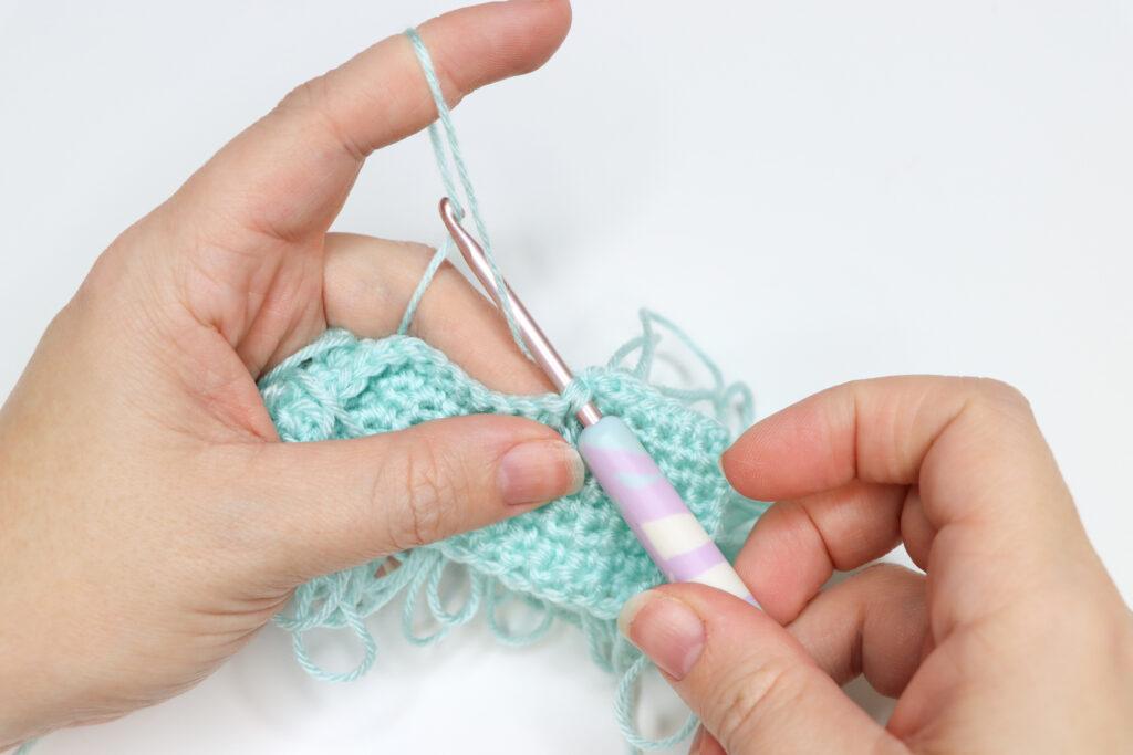 An in progress swatch of loop crochet stitch in aqua yarn.