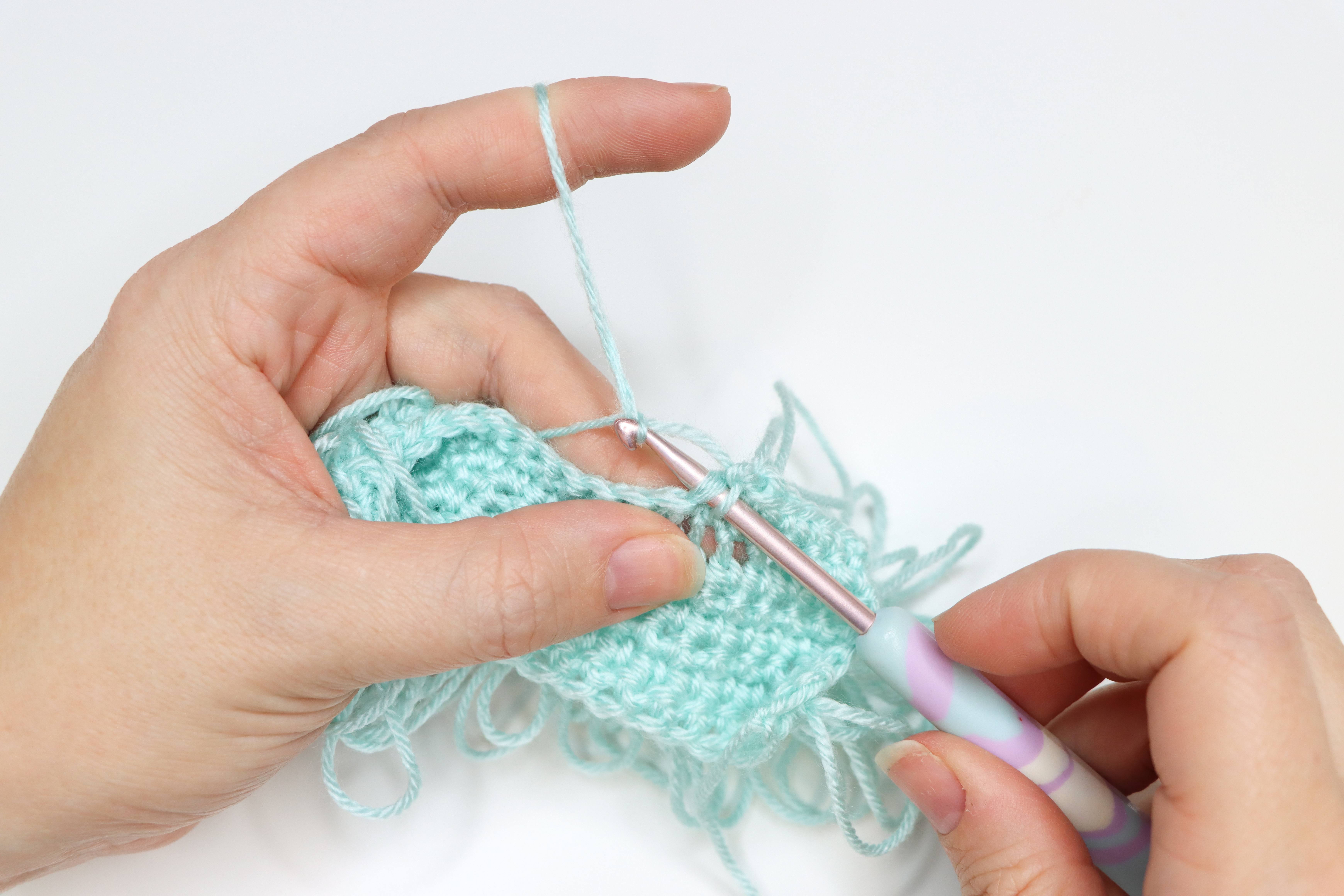 An in progress swatch of loop crochet stitch in aqua yarn.