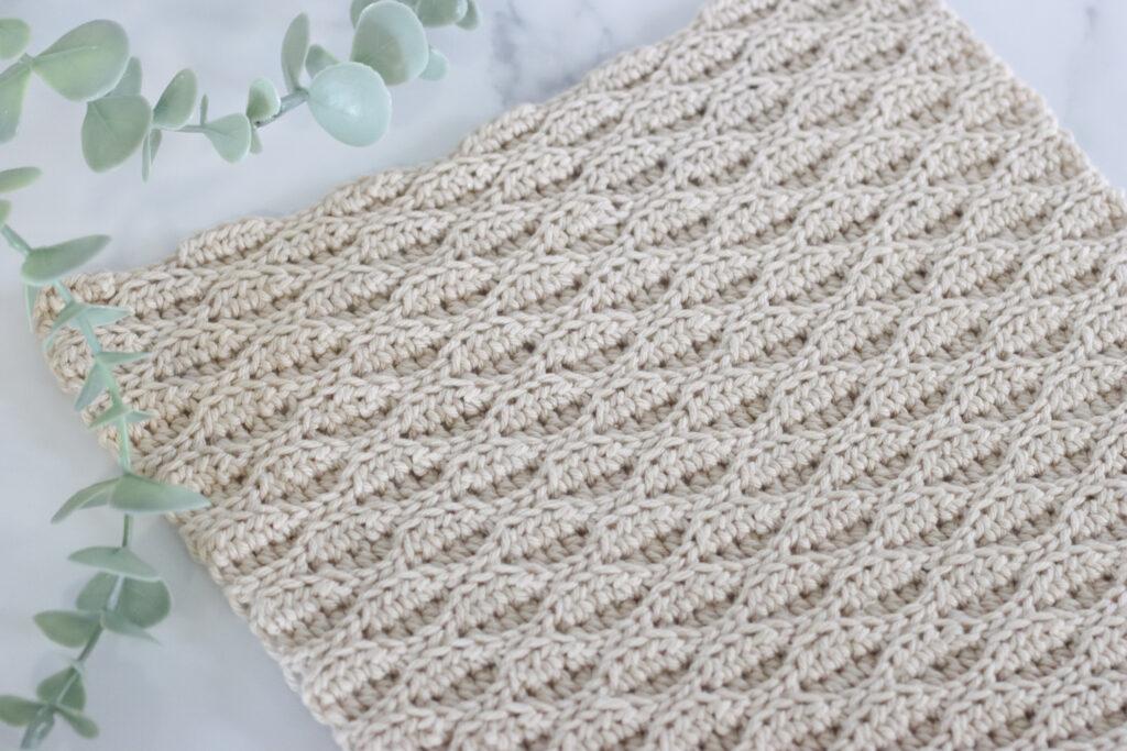 Almond Ridges crochet swatch on a marble background with a plant.