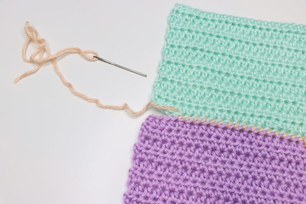 A pair of female hands is shown demonstrating how to to the whipstitch. The swatch is purple, aqua and peach, bright colours so that the stitching is clearly demonstrated.