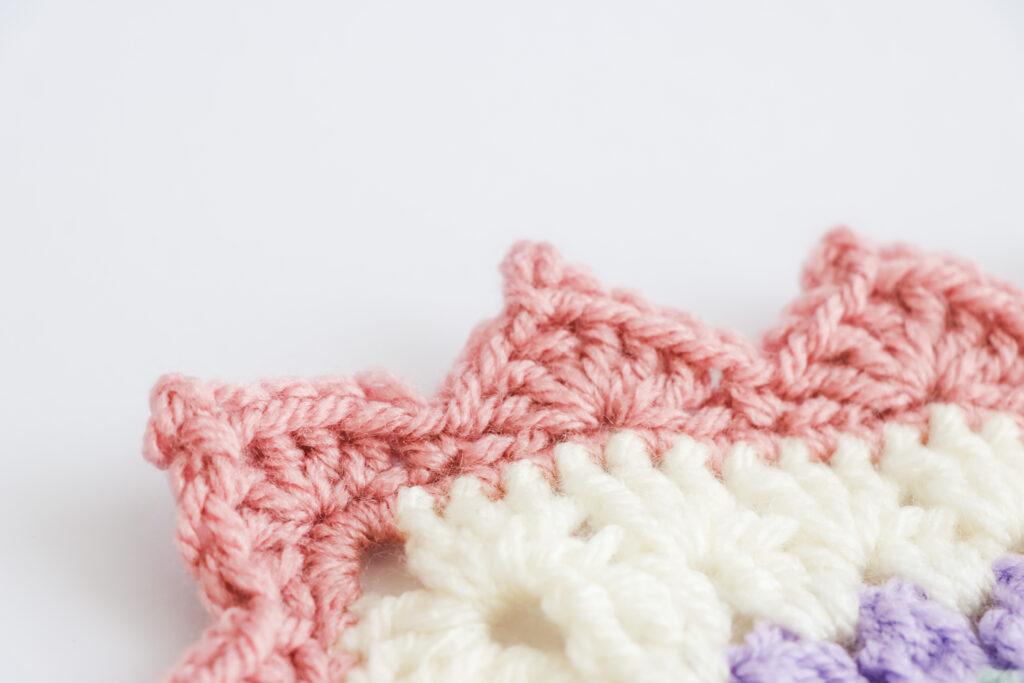 A swatch of triangle picot edge border is displayed. The swatch is made from white yarn with the border made from a dusty rose colour.