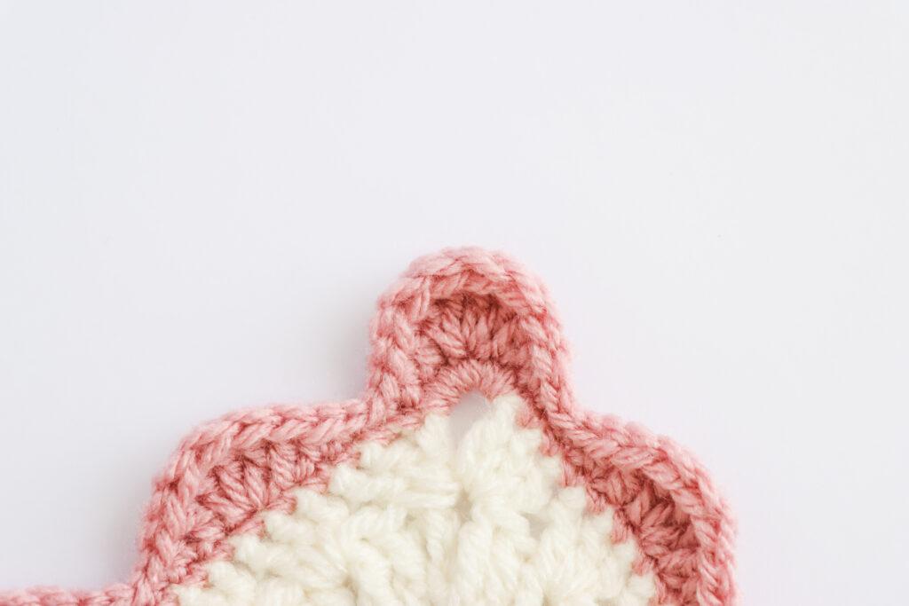 A swatch of wavy edge border is displayed. The swatch is made from white yarn with the border made from a dusty rose colour.