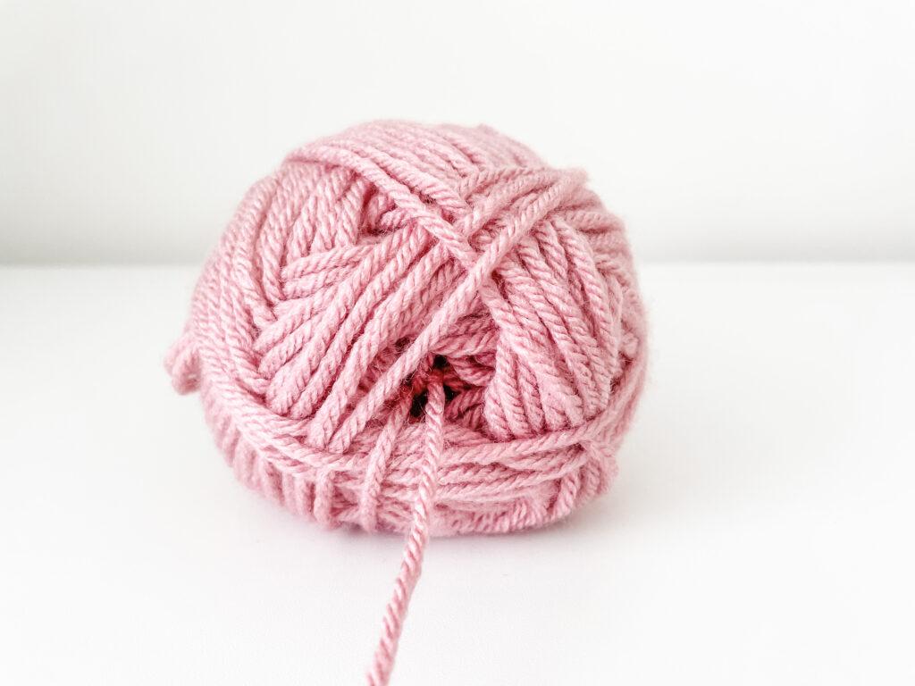 A ball of dusty pink Stylecraft Special yarn sits on a white surface. The yarn is being pulled from the centre.