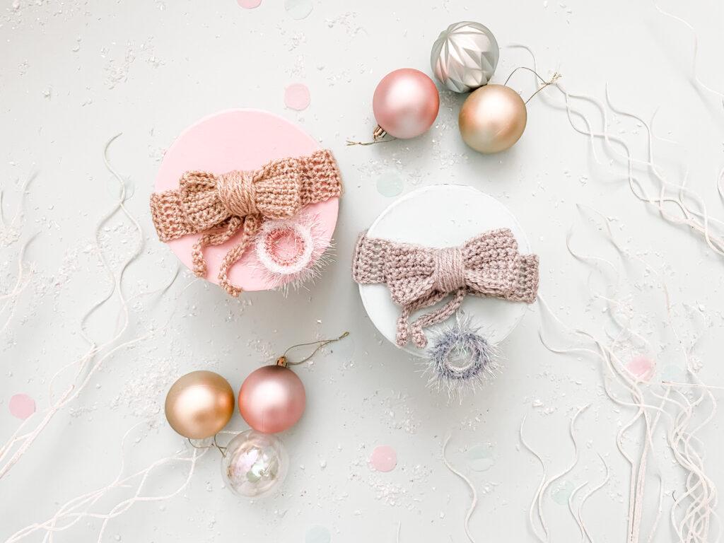 flat lay image to shwo two pastel coloured round boxes wrapped in crochet ribbon with a crochet bow and present topper surrounded by sparkly silver branches and pastel coloured baubles.