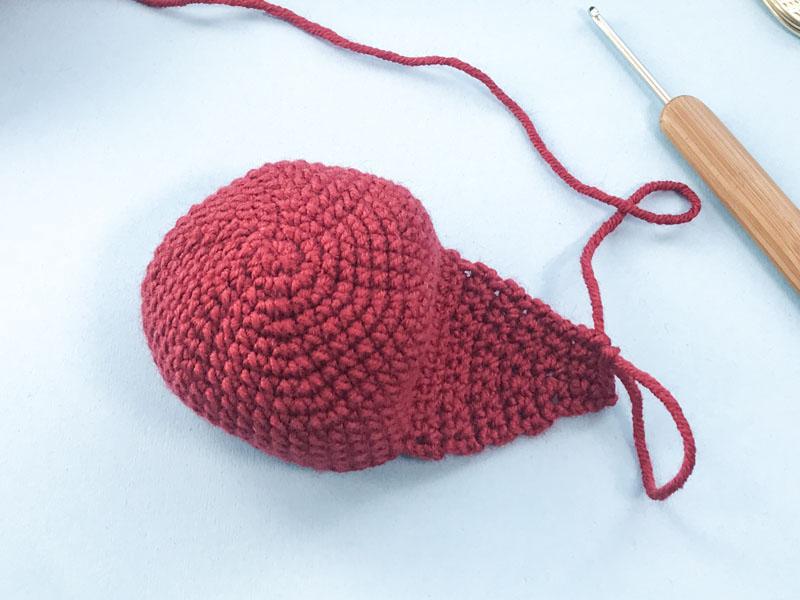 Red coloured yarn creating the face of the fox is show next to a wooden crochet hook.