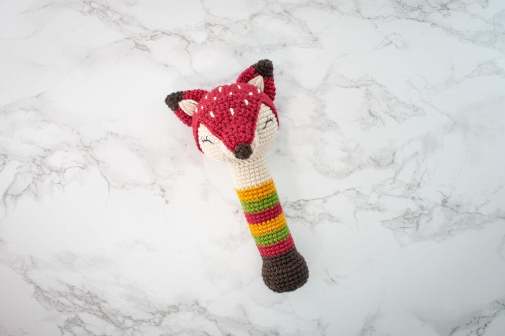 Amigurimi Rattle in the shape of a Fox shown on a white marble background.