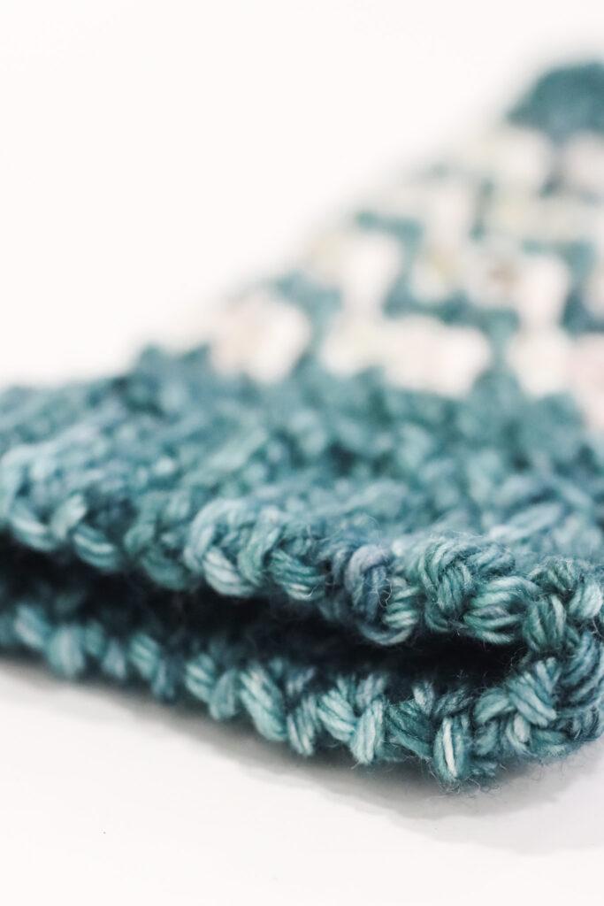 a close image of a crochet wrist warmer cuff in green indie dyed yarn.