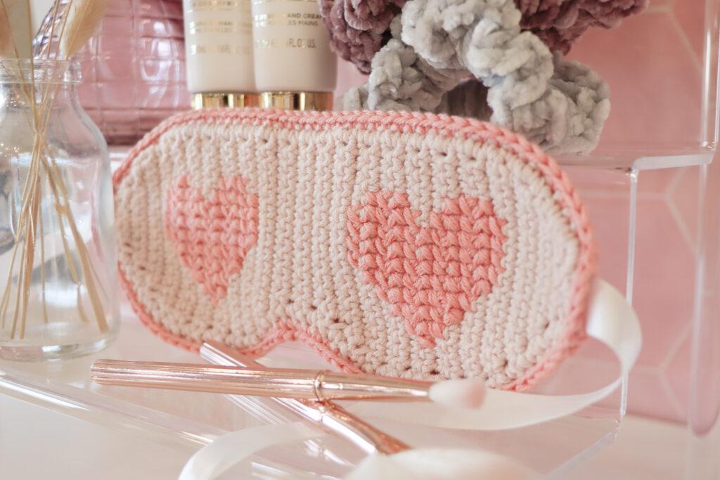 Crochet eye mask surrounded by other self care items such as scrunchies, make up brushes and beauty creams