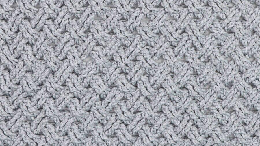 Close-up of a crochet fabric made with the Celtic Weave stitch in light grey yarn, showing an interlocking, textured pattern resembling braided cables.