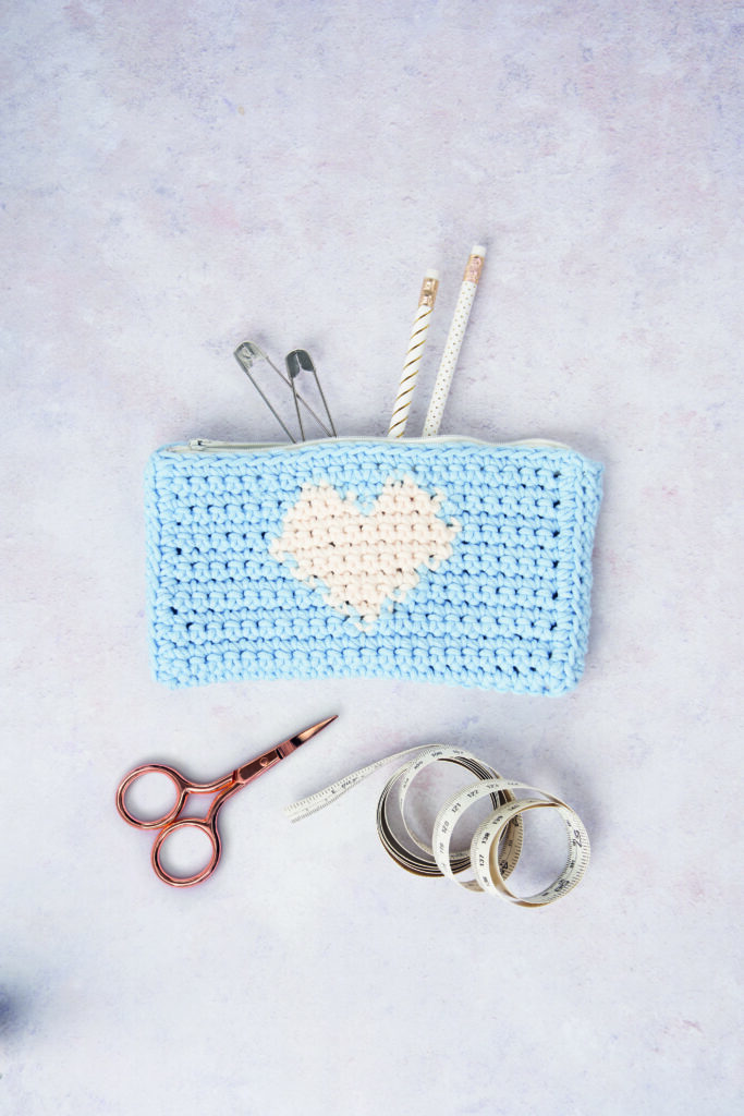A blue pencil case featuring a white heart with stationery coming out of it photographed as a flat lay.