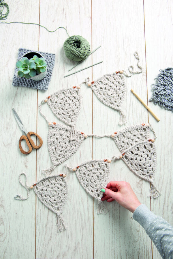 crochet triangle bunting in a granny triangle style with wooden hooks, beads and yarn on a wood plank background