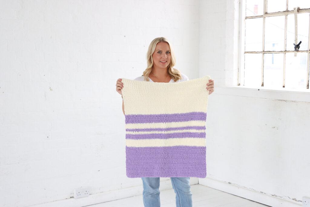 Switch It Up Blanket held by Sarah-Jayne in a white room.