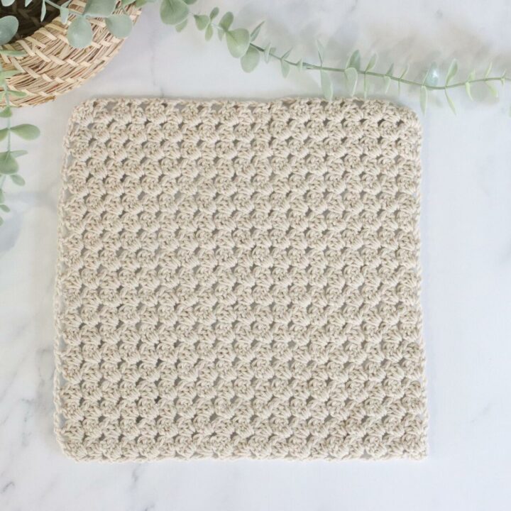 A corner to corner granny square on a plain background made with oatmeal coloured yarn.