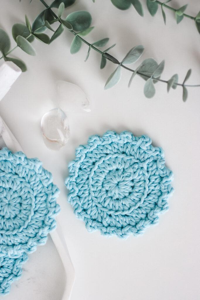 flat lay image of blue face scrubbies on a white background with green foliage at the top of the image.