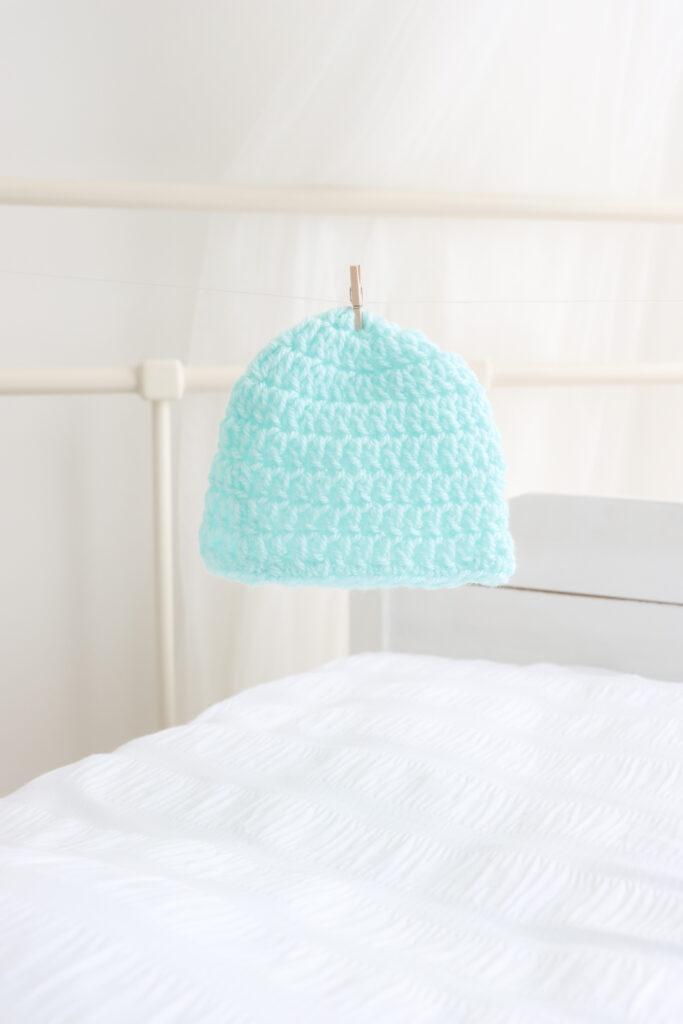a turquiose baby beanie pegged on a fishing line in a white bedroom setting