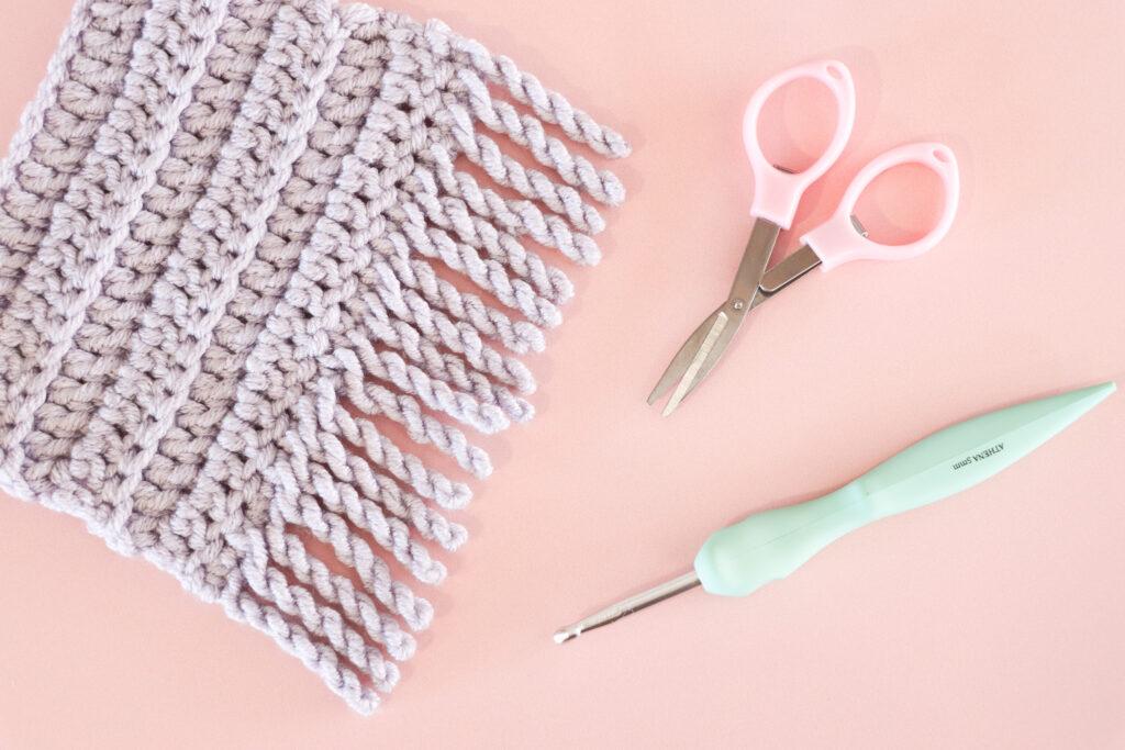 A crochet fringe border with pink scissors and mint green crochet hook.