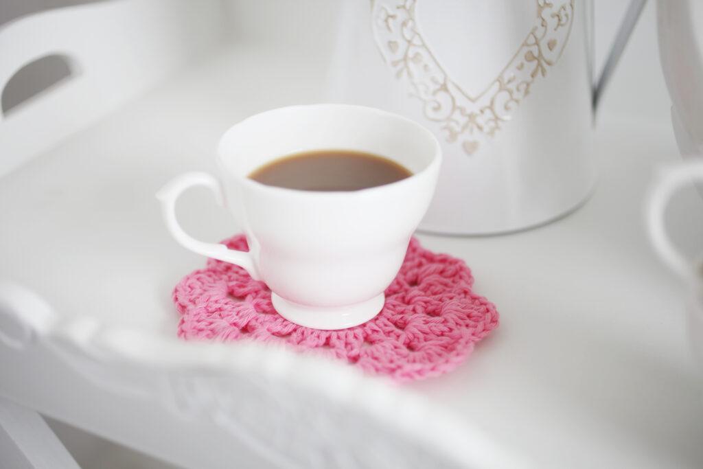 a pink crochet coaster on a white tray with a white cup of coffee on it.