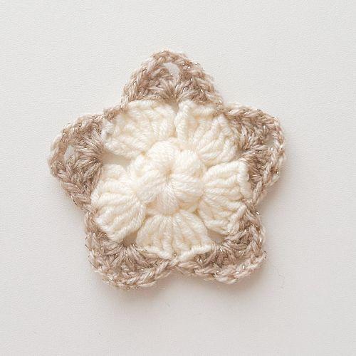 a flat lay image of a crochet star made using a cream cotton DK yarn for the first two rounds and a sparkly DK yarn to show how this pattern looks when you change colour for the final round.